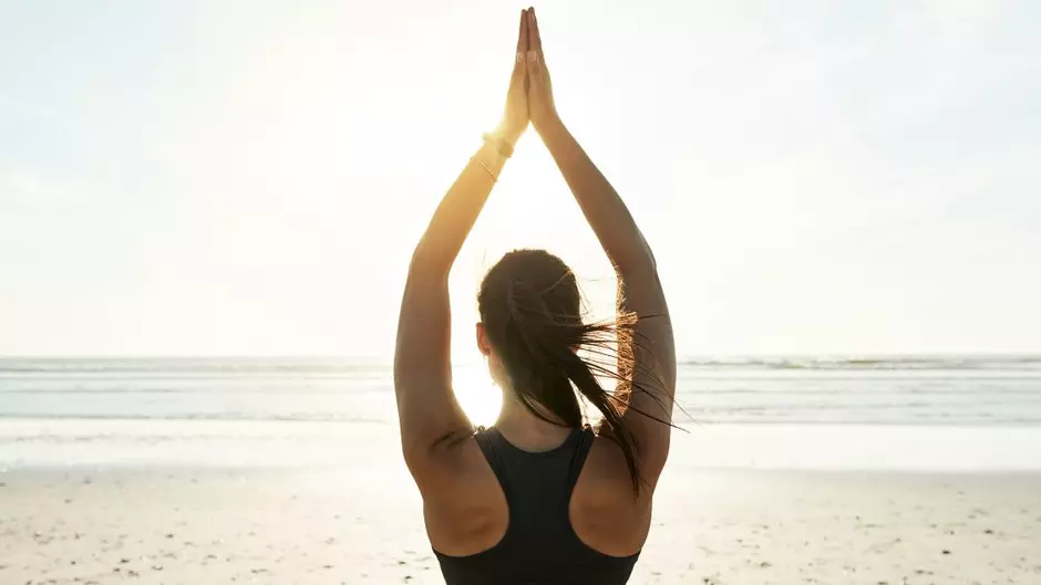 A woman stands on a beach with her hands above her head