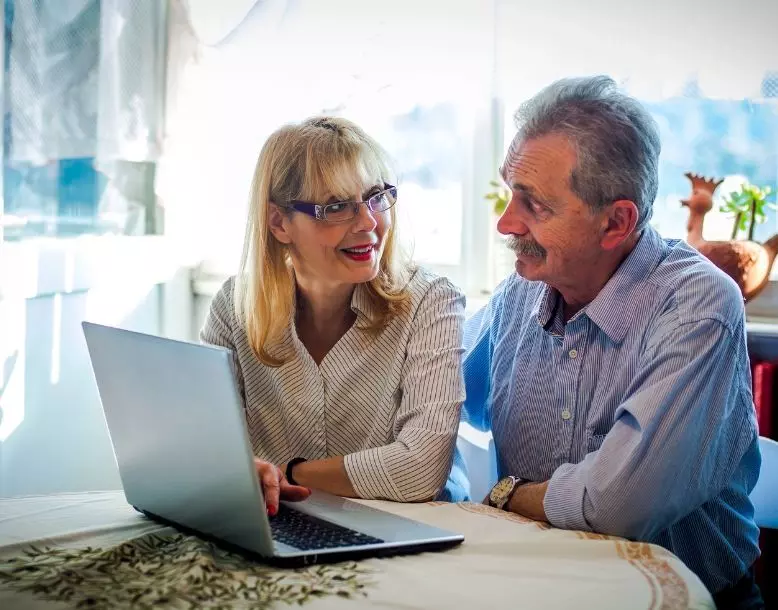 A couple reviews documents on their computer at home