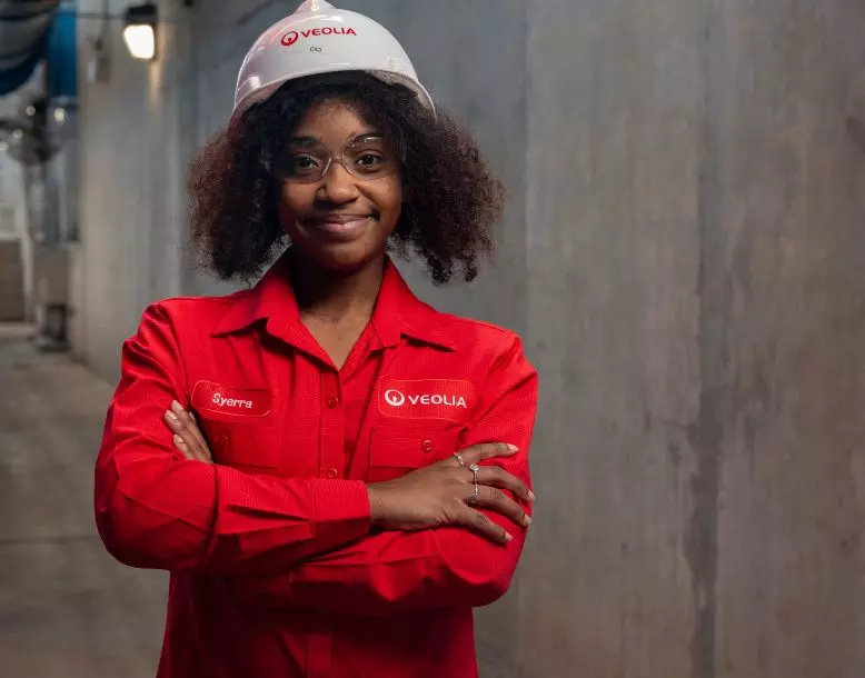 A Veolia employee smiles for the camera wearing a hard hat and protective glasses 