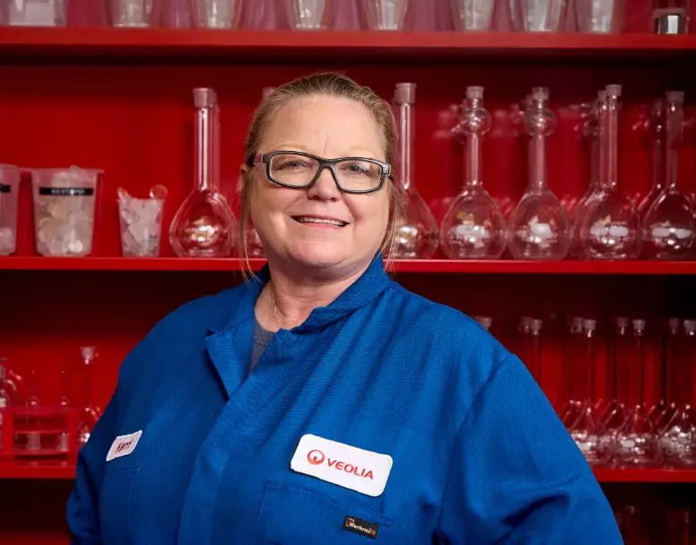 A Veolia employee smiles for the camera with shelves of glass lab equipment in the background